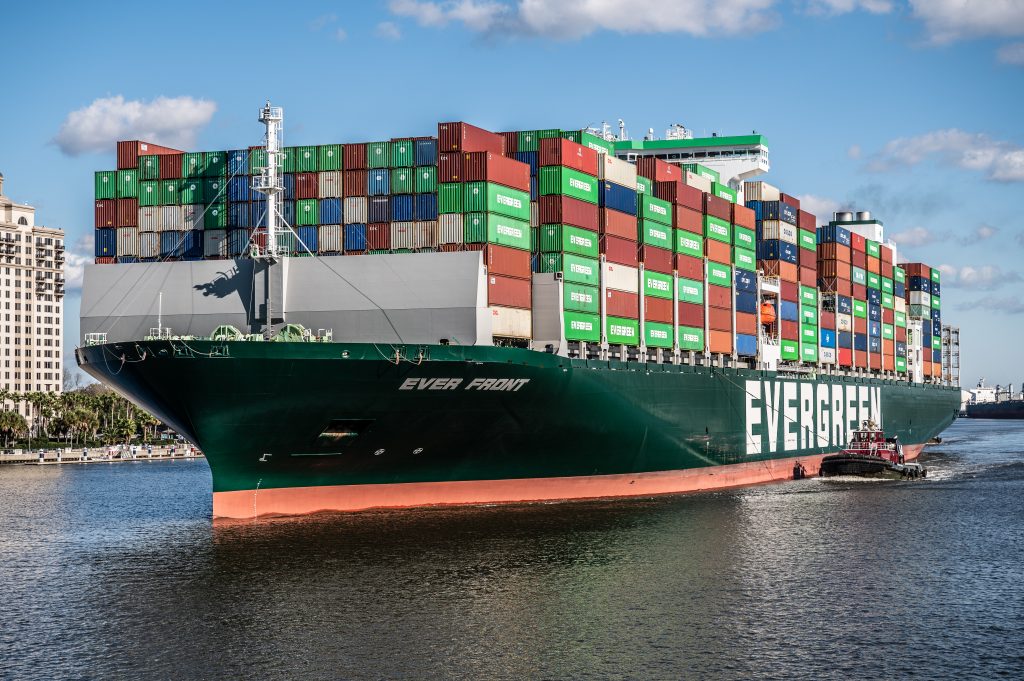 Ein großes Containerschiff im Hafen mit der Aufschrift Evergreen, gezogen von einem Schlepper.