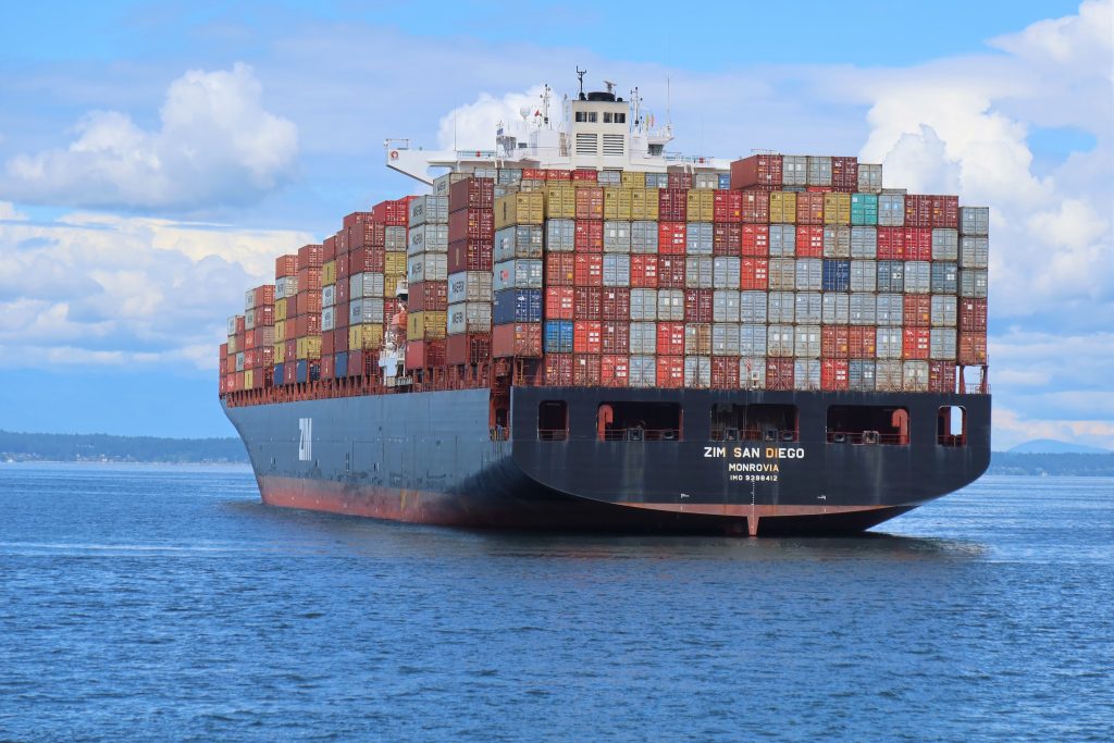 Large container ship on the sea, blue sky and land in the background.