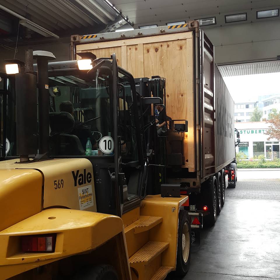 Large wooden container being loaded into a sea container by a forklift driver.